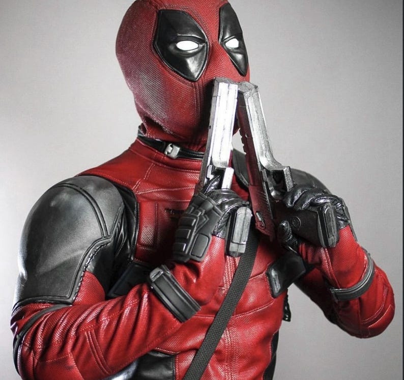 May include: A red and black Deadpool costume with a mask, holding two silver toy guns. The costume features a textured red leather-like material with black accents on the shoulders and gloves. The mask has white eye cutouts.