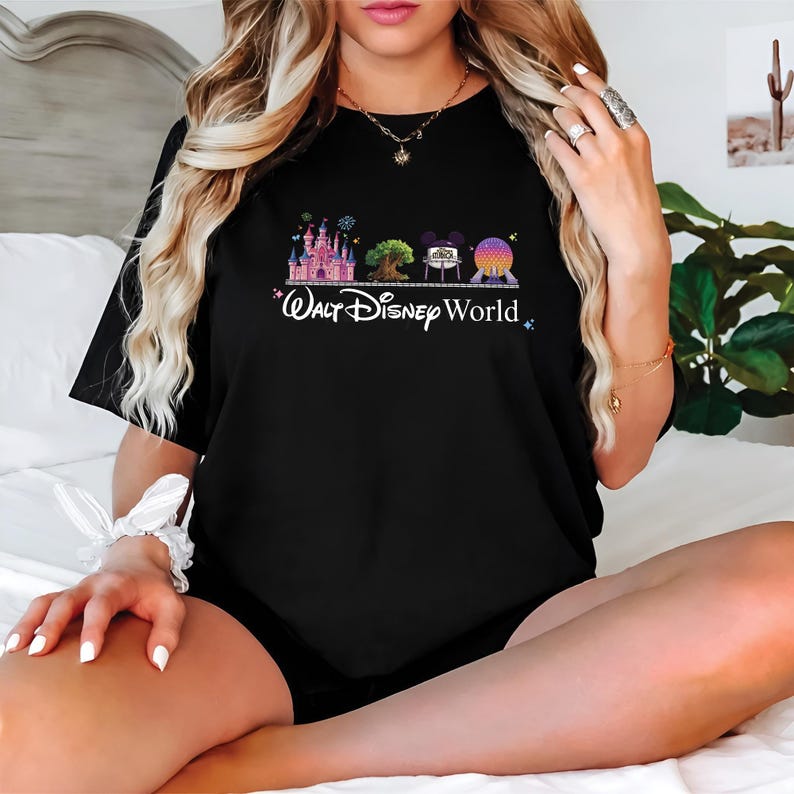 May include: Black t-shirt featuring a colorful graphic of Disney World icons, including a castle, tree, and Spaceship Earth. The words "Walt Disney World" are written in white script below the graphic. The shirt is a classic crew neck.