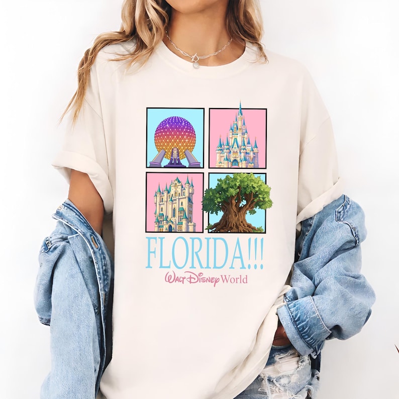 May include: Cream-colored t-shirt featuring four square illustrations of Florida landmarks. The shirt includes the text "FLORIDA!!!" in light blue, with "Walt Disney World" below in a smaller font. The illustrations include a sphere, a castle, and a tree.