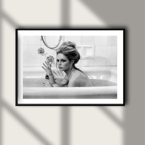 May include: Black and white framed photograph of a woman in a bathtub. The woman is looking at the camera with her hand raised. The photograph is in a black frame.