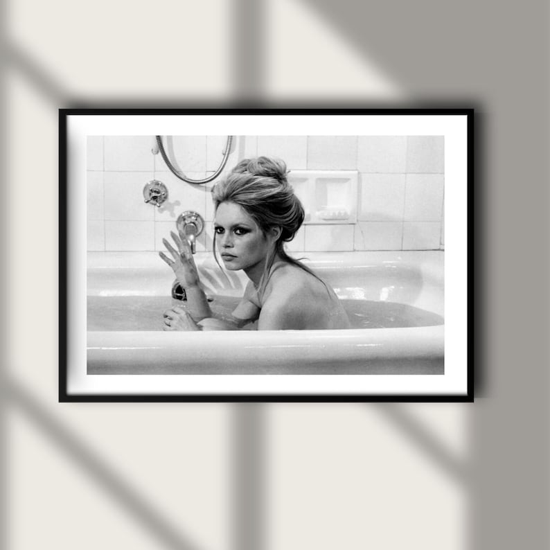 May include: Black and white framed photograph of a woman in a bathtub. The woman is looking at the camera with her hand raised. The photograph is in a black frame.