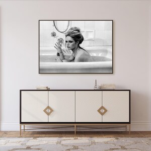 May include: Black and white framed photograph of a woman in a bathtub. The photograph is mounted above a white and black cabinet with gold accents. The cabinet has a diamond pattern on the doors.
