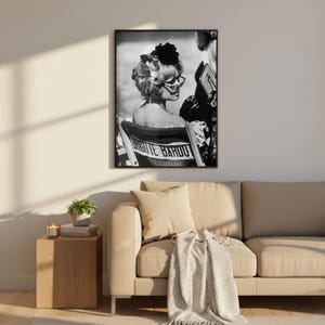 Pu&ograve; includere: Stampa incorniciata in bianco e nero di Brigitte Bardot seduta su una sedia da regista. La sedia ha il nome "Brigitte Bardot" stampato sopra. Indossa occhiali da sole e un fiore scuro tra i capelli.