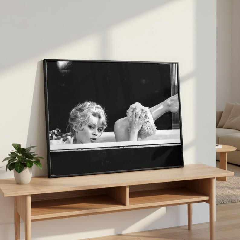 Puede incluir: Impresi&oacute;n enmarcada en blanco y negro que representa a una mujer en una ba&ntilde;era. La imagen tiene una est&eacute;tica vintage, mostrando el rostro y la parte superior del cuerpo de la mujer. Otra persona se lava la pierna con una esponja.