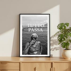 May include: Monochrome framed print showing a man smoking with the words "TUTTO PASSA" above. The man is shirtless, wearing sunglasses, and has a tattoo that says "TUTTO PASSA". The background depicts water and a mountain.