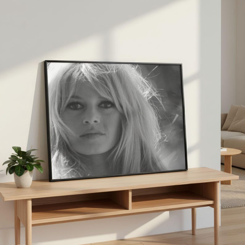 Pode incluir: Impress&atilde;o emoldurada em preto e branco de uma mulher com cabelo loiro comprido e solto. O retrato &eacute; exibido em uma mesa de console de madeira clara, com uma pequena planta em vaso &agrave; esquerda. O quarto tem uma paleta de cores neutras.