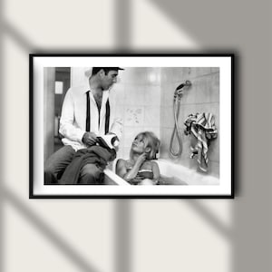 May include: Black and white framed print featuring a vintage photograph of a man and a woman in a bathroom setting. The woman is in a bathtub, and the man is leaning against the tub.