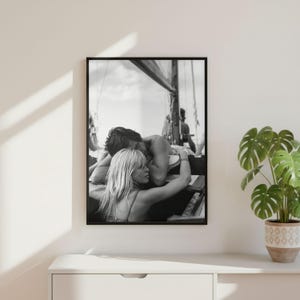 以下が含まれることがあります： ボート上で抱き合うカップルの白黒フレーム写真。男性が女性に寄り添う、二人の間の優しい瞬間を捉えた画像です。背景にはボートの構造と別の人物が写っています。