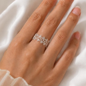 May include: A silver-toned ring featuring an intricate, openwork lace-like pattern that wraps around the band. The metal has a polished finish, and the design consists of repeating geometric shapes that create a delicate, airy appearance on the finger.