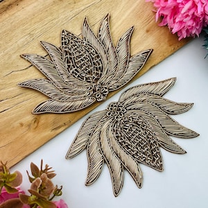 以下が含まれることがあります： 金属光沢のあるゴールドの刺繍が施された蓮の花のアップリケ2枚。ワイヤーのような複雑な糸使いと、詳細な花びらの模様が特徴です。それぞれのピースは、中央に織り込まれたテクスチャがあり、その周囲に放射状に伸びる尖った花びらが配置されています。