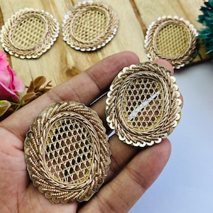 May include: Close-up of several gold-coloured, oval-shaped embellishments. Each has a woven centre, a beaded border, and a twisted rope-like edge. The embellishments are on a light-coloured wooden surface.