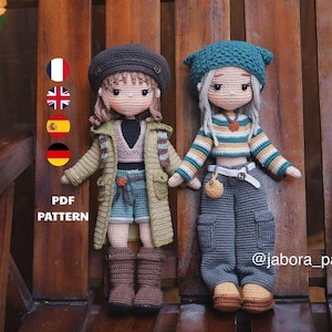 Pode incluir: Duas bonecas de crochê com cabelo de fio e roupas detalhadas. A boneca da esquerda usa uma boina marrom, casaco oliva e botas marrons. A da direita usa um gorro azul-petróleo, blusa listrada de manga comprida e calças cargo cinzas.