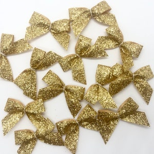 May include: A collection of 12 gold glitter bows. The bows are arranged in a circular pattern on a white background.