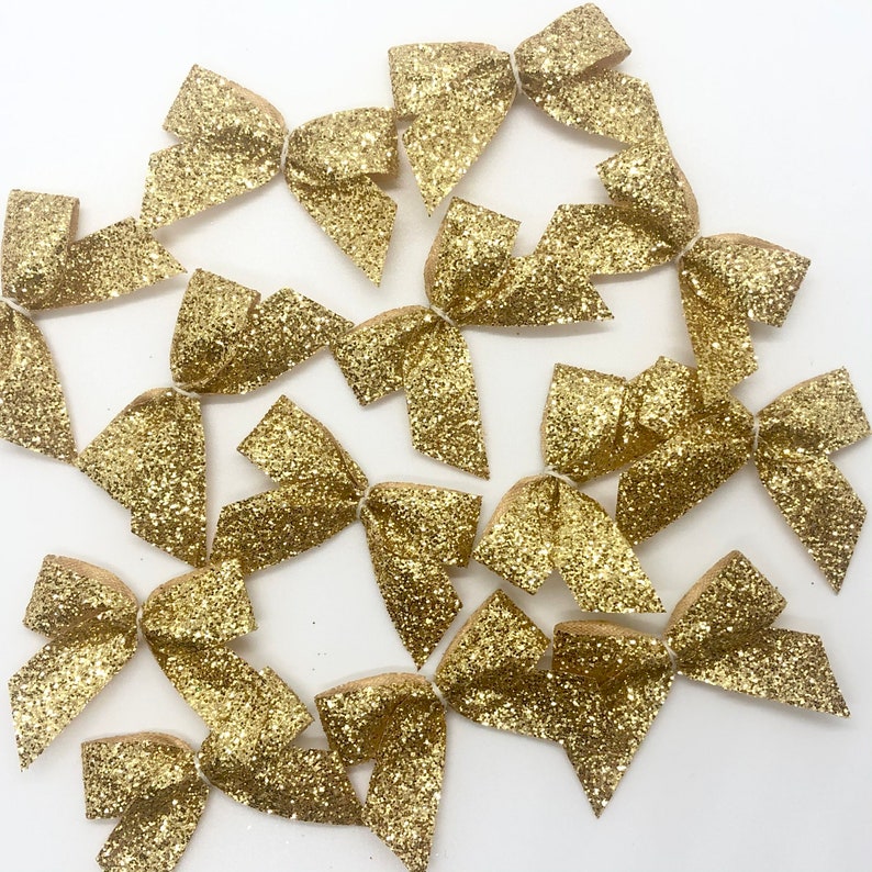 May include: A collection of 12 gold glitter bows. The bows are arranged in a circular pattern on a white background.