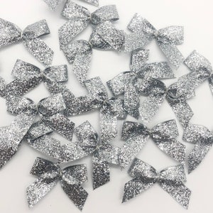 May include: A pile of silver glitter bows. The bows are made of a sparkly material and are perfect for adding a touch of sparkle to any craft project.