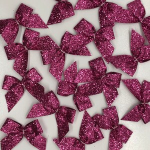 May include: A collection of small, sparkly, magenta bows. The bows are made of a glittery fabric and are perfect for adding a touch of sparkle to any project.