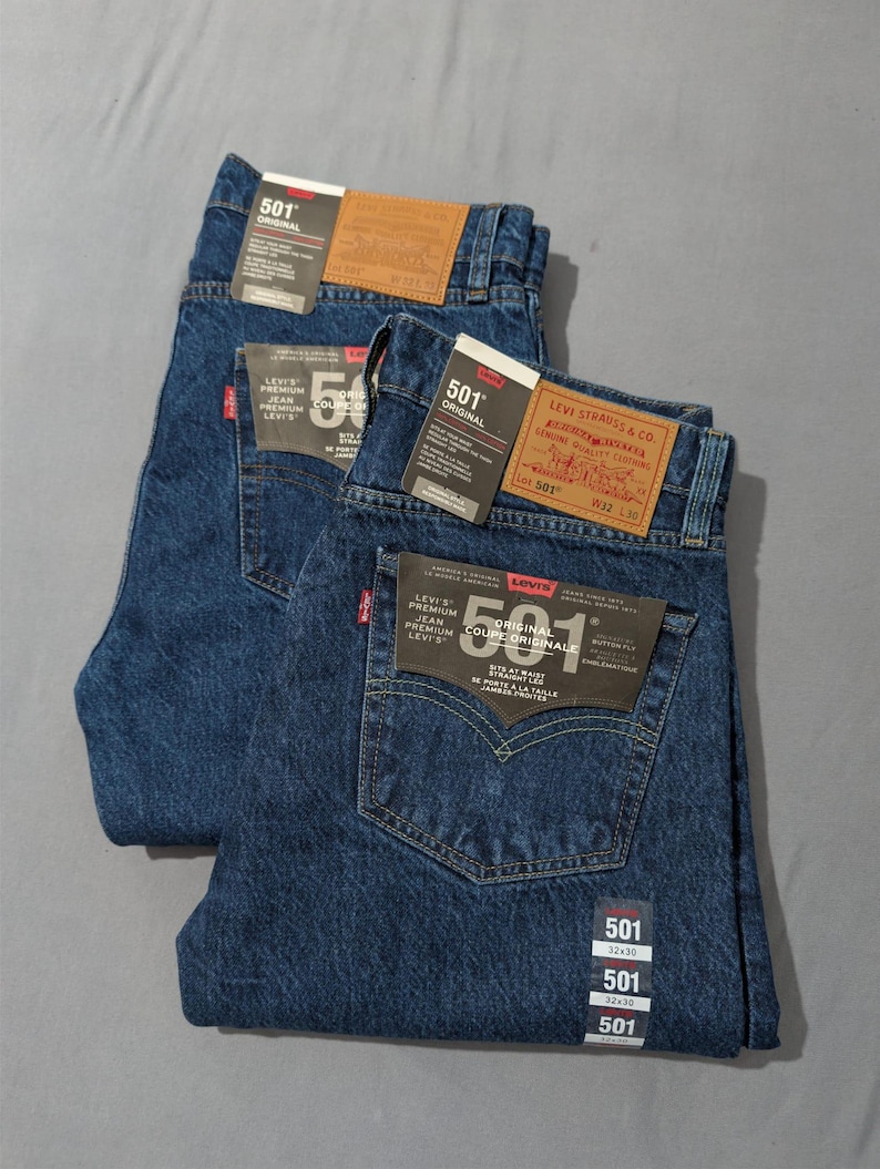 May include: Two pairs of dark blue Levi's 501 Original jeans. Each pair has a classic five-pocket design, a button fly, and the Levi's brand label on the back. The jeans have tags with the size 32x30.