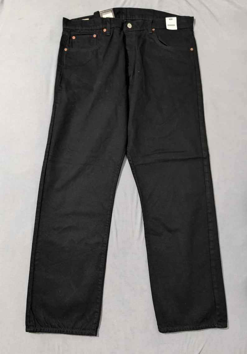May include: Black denim jeans with a classic five-pocket design. The jeans have a button and zipper closure, belt loops, and copper rivets. The garment is laid flat on a light gray surface.