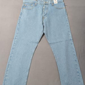 May include: Light blue denim jeans with a button fly and classic five-pocket design. The jeans are new, with tags attached, and have a relaxed fit. The light wash denim is a classic style.