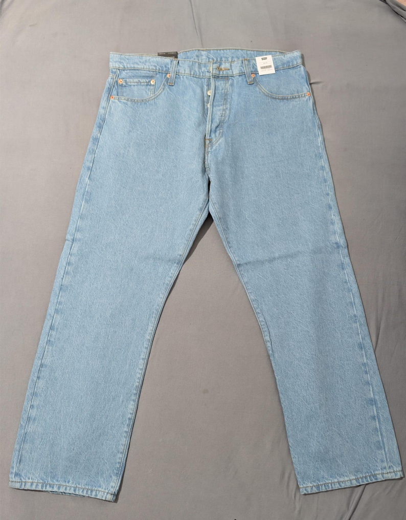 May include: Light blue denim jeans with a button fly and classic five-pocket design. The jeans are new, with tags attached, and have a relaxed fit. The light wash denim is a classic style.