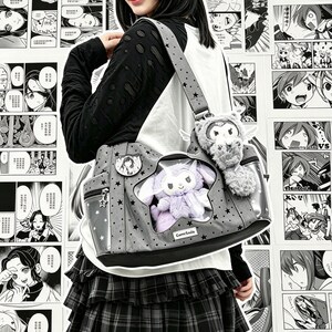 May include: A grey shoulder bag featuring a star-shaped clear window displaying a light purple plush character. The bag is decorated with black star patterns, a small circular pin, a grey plush charm, and a label with the text GameSoda.