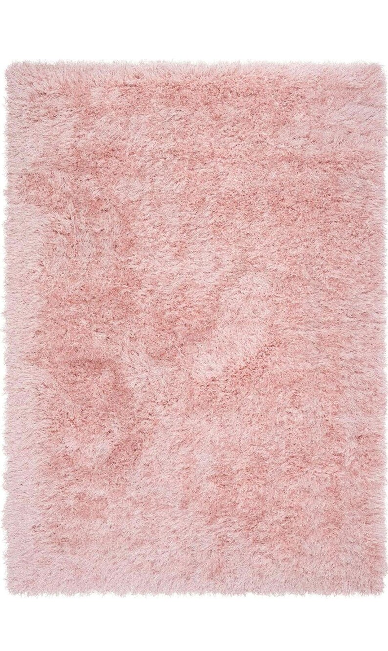 Peut inclure: Un tapis rectangulaire rose clair, avec une texture dense et duveteuse. Les longs brins de fibres cr&eacute;ent un aspect doux et accueillant. La couleur rose p&acirc;le est uniforme, offrant une sensation de confort et de chaleur. Id&eacute;al pour une chambre.