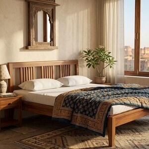 May include: A wooden bed frame with a headboard featuring vertical slats. The bed is made up with white pillows and a blue and gold patterned quilt. A wooden nightstand with a lamp and a decorative mirror are also visible.