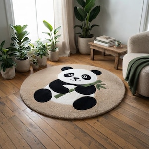 Op de afbeelding: Een rond, beige vloerkleed met een centraal getuft ontwerp van een zwart-witte panda die een groene bamboestengel vasthoudt. Het kleed heeft een zacht, getextureerd oppervlak en ligt op een houten vloer in een kamer met diverse planten.