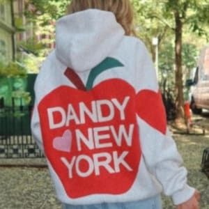 Könnte beinhalten: Weißer Kapuzenpullover mit einem großen roten Apfel-Grafik auf dem Rücken. Das Apfel-Design enthält ein grünes Blatt, ein rosa Herz und die Worte "DANDY NEW YORK" in weißen Blockbuchstaben.
