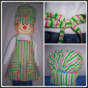May include: A green and pink striped chef hat and apron set with rainbow trim. The hat and apron are made of fabric with a striped pattern.