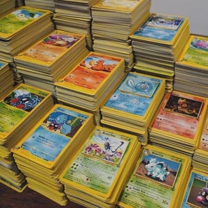 May include: A large collection of rectangular trading cards featuring colorful illustrations of various creatures and characters. The cards are organized into multiple tall, neat stacks, each with yellow borders and printed text details.