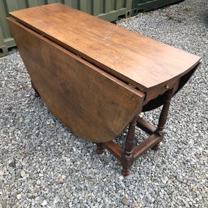 Puede incluir: Mesa de alas de madera con un acabado marrón cálido. La mesa tiene una tapa rectangular con bordes redondeados y una hoja abatible a cada lado. Se apoya sobre cuatro patas torneadas, y mide unos 76 cm de largo cuando está cerrada.