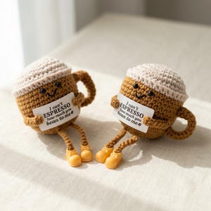 Puede incluir: Dos figuras de tazas de caf&eacute; de ganchillo con caras sonrientes, sosteniendo carteles que dicen "I can't ESPRESSO how much you bean to me". Las tazas son marrones con bordes y asas color canela, y tienen piernas color canela y zapatos amarillos.
