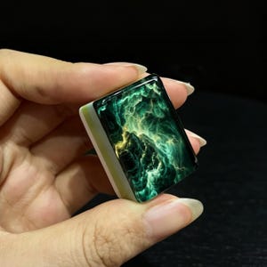 May include: A rectangular mahjong tile featuring a glossy, dark green and black surface with swirling, nebula-like patterns in shades of bright yellow and lime green. The base of the tile is a solid, opaque white material with a thin light green stripe.