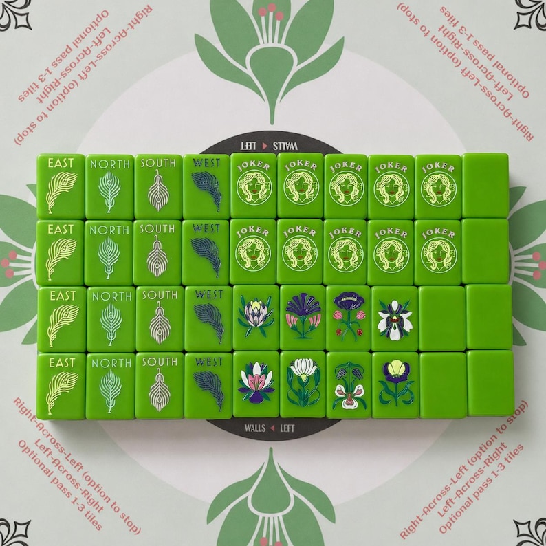 May include: A set of green Mahjong tiles arranged in a grid on a patterned surface. The tiles feature engraved designs of feathers, the words EAST, NORTH, SOUTH, WEST, the word JOKER with a face illustration, and various colorful floral motifs.