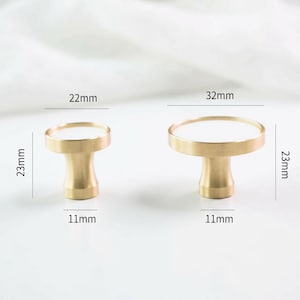Puede incluir: Dos tiradores de armario de lat&oacute;n con tapas blancas. El tirador m&aacute;s peque&ntilde;o mide 2,3 cm de alto, 2,2 cm de ancho y 1,1 cm de profundidad. El tirador m&aacute;s grande mide 2,3 cm de alto, 3,2 cm de ancho y 1,1 cm de profundidad.