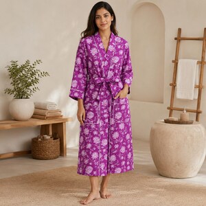 May include: A vibrant purple robe featuring a white floral pattern, long sleeves, a tie-waist belt, and two front patch pockets. The garment is finished with white piping along the lapels, cuffs, and pockets, creating a structured look.