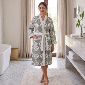 May include: A knee-length robe featuring a sage green and white scalloped pattern with floral motifs. The garment includes long sleeves, a white shawl collar, a matching tie belt at the waist, and two front patch pockets with white trim.