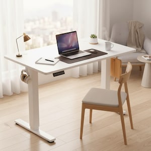 May include: A white adjustable standing desk with a laptop, mouse, and notepad. A small desk lamp and headphones are on the desk. A wooden chair with a gray cushion is in front of the desk. A small plant in a white pot is on the desk.