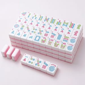 May include: A complete Mahjong set with white tiles featuring colorful symbols and characters. The tiles have pink accents and are stacked neatly. Several spare tiles are arranged separately, ready for play.