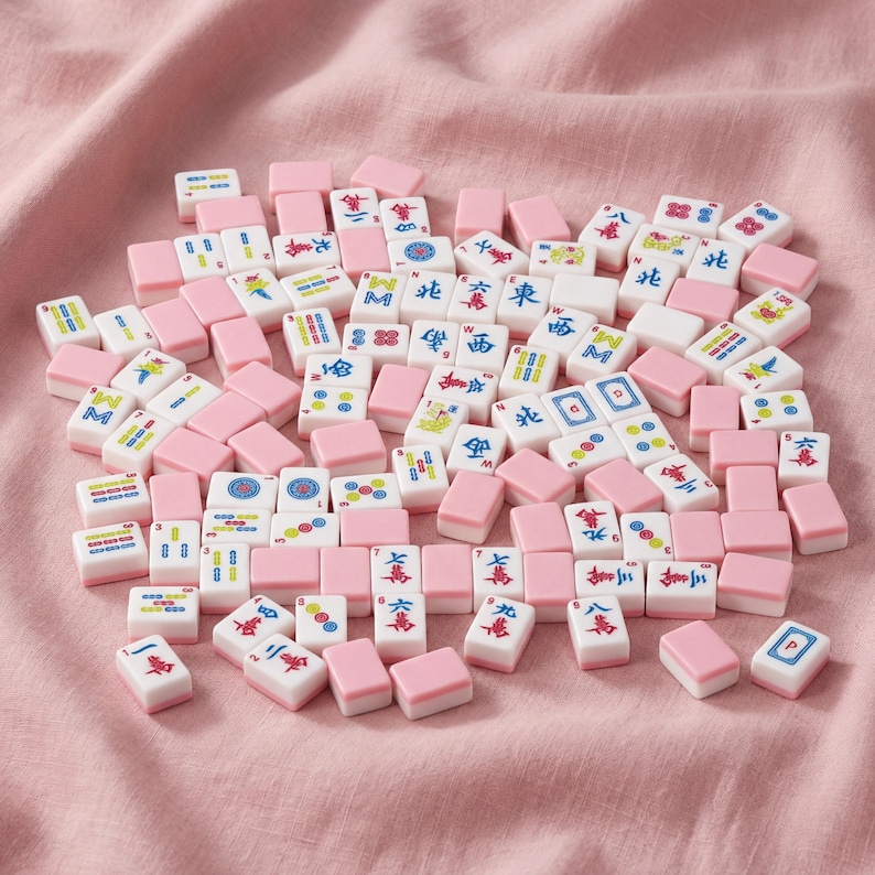 May include: A collection of pink and white Mahjong tiles scattered on a pink fabric surface. The tiles feature various symbols and characters in red, blue, and green. The pink tiles are rectangular and serve as the base for the white tiles.