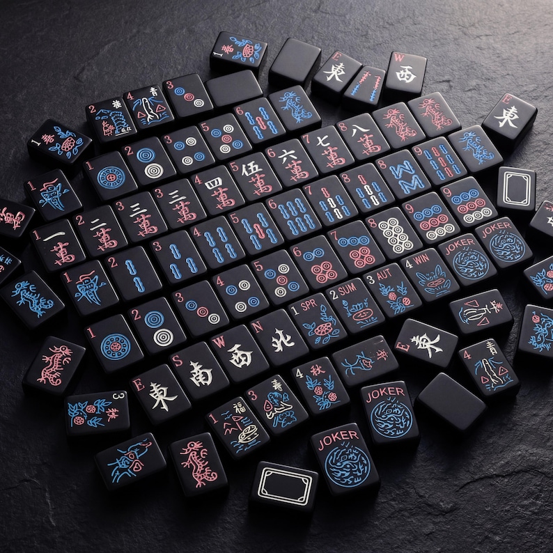 K&ouml;nnte beinhalten: Eine Sammlung schwarzer Mahjong-Steine mit roten, blauen und wei&szlig;en Symbolen und Schriftzeichen. Die Steine sind auf einer dunklen Oberfl&auml;che angeordnet und zeigen verschiedene Anz&uuml;ge, Zahlen und Spezialsteine wie "Joker".