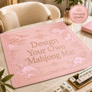 May include: A square, light pink mahjong mat featuring an embossed border with traditional cloud and pine tree motifs. The center displays the text "Design Your Own Mahjong Mat" in a serif font, accompanied by a circular emblem and geometric corner patterns.