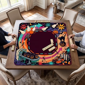 May include: A square game mat featuring a vibrant Halloween-themed illustration with ghosts, jack-o'-lanterns, skeletons, and bowling elements. The design includes a dark central area for gameplay, surrounded by colorful graphics and scattered game tiles.