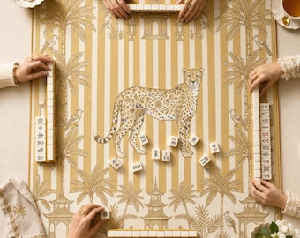 Op de afbeelding: Een vierkante mahjongmat met een goud-wit gestreept patroon, voorzien van illustraties van palmbomen, vogels en pagodes. Een grote jachtluipaard met een bloemmotief op het lichaam staat centraal op de mat, omringd door verspreide mahjongtegels.