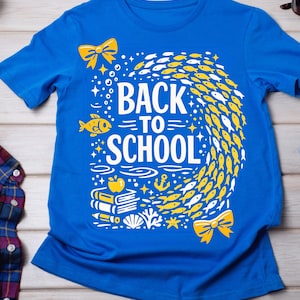 Peut inclure: Un t-shirt bleu vif à manches courtes avec une impression graphique blanche et jaune. Le motif comprend le texte "BACK TO SCHOOL" entouré d'un banc de poissons, de livres, d'une pomme, d'une ancre, de coquillages et de deux nœuds jaunes.