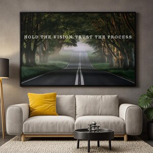 May include: A rectangular wall art print in a black frame featuring a dark, foggy road winding through a dense forest of green trees. The text HOLD THE VISION, TRUST THE PROCESS is printed in white capital letters across the centre of the image.
