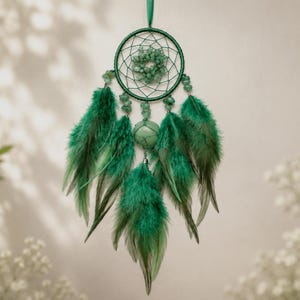 Könnte beinhalten: Ein grüner Traumfänger mit einem kreisförmigen Reifen, der mit dunkelgrünem Faden umwickelt ist und ein gewebtes Netz in der Mitte aufweist. Das Design umfasst kleine grüne Steinperlen, eine größere zentrale Steinperle und hängende Federn.