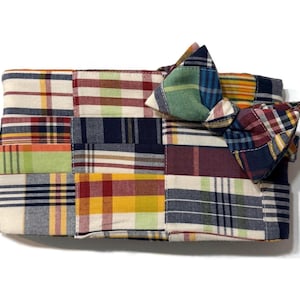 May include: A patchwork clutch with a bow, featuring a variety of plaid patterns in colors like red, blue, green, and yellow. The rectangular clutch has a zipper closure and a matching bow accent.