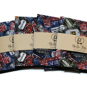 May include: Four pocket squares with a patriotic theme. The pocket squares feature a variety of military and American flag designs. The pocket squares are made of fabric and have a blue, red, white, and green color scheme. The pocket squares are packaged with a brown paper tag that says "HoBo Ties" and "shopHoBoTies.com".